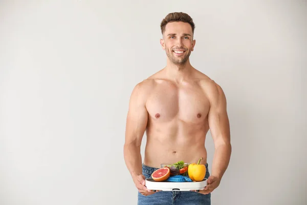 Handsome muscular man with scales and healthy food on light background. Weight loss concept — Stock Photo, Image