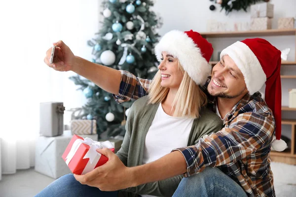 Pareja feliz en Santa sombreros tomando selfie en casa en la víspera de Navidad — Foto de Stock