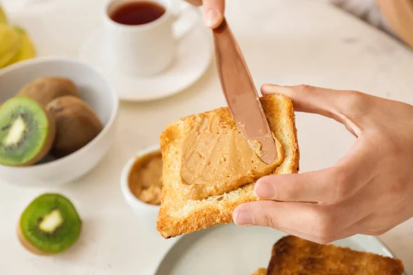 Woman spreading tasty peanut butter onto toasted bread, closeup — Stock Photo, Image