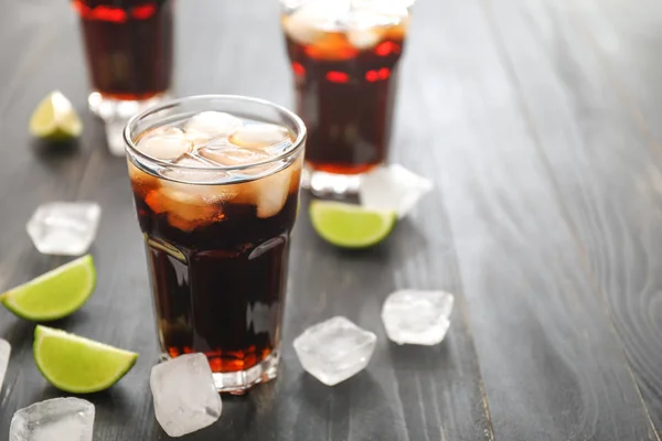 Copos de cola fria, cubos de gelo e limão na mesa de madeira — Fotografia de Stock