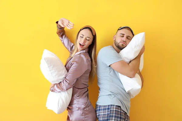 Sleepy young couple with pillows on color background — Stock Photo, Image