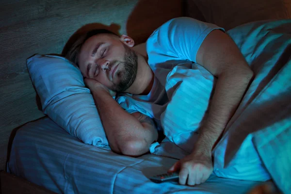 Молодой человек с пультом от телевизора спит в постели по ночам — стоковое фото