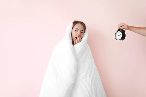 Sleepy young woman wrapped in blanket and male hand with alarm clock on color background — Stock Photo, Image