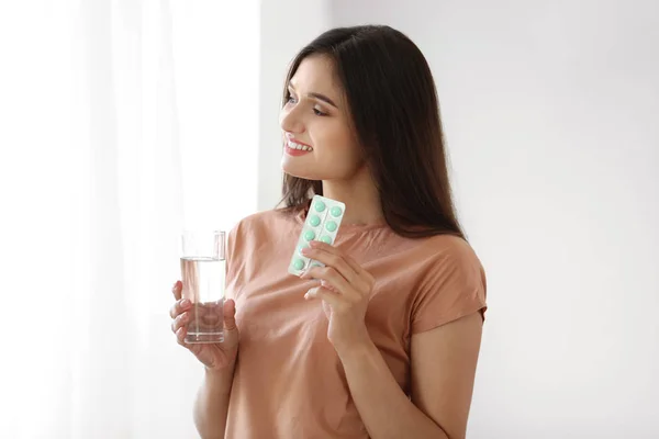 Mladá žena s tabletky a sklenicí vody doma — Stock fotografie