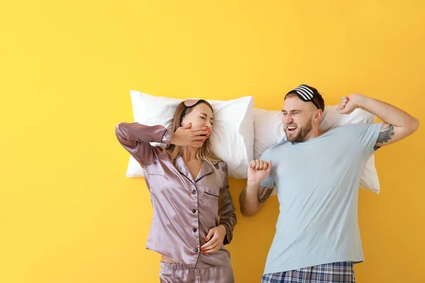 Pareja joven y somnolienta con almohadas sobre fondo de color — Foto de Stock