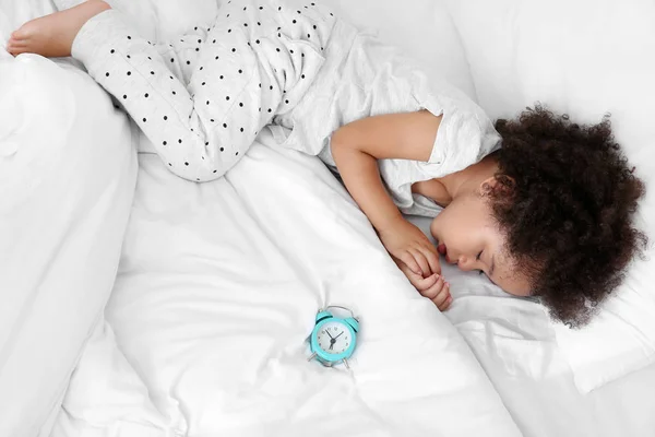 Little African-American girl with alarm clock sleeping in bed — Stock Photo, Image