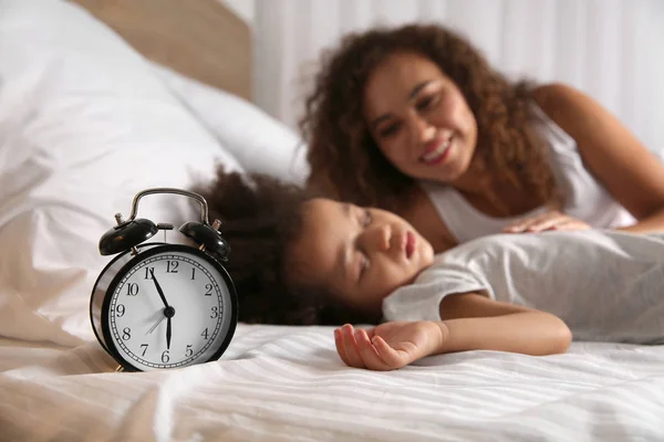 African-American mother with sleeping daughter and alarm clock on bed at night — Stock Photo, Image