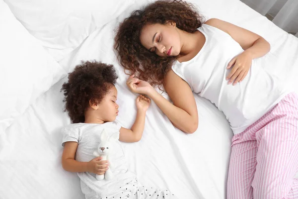 Annesi yatakta uyuyan küçük Afrikalı-Amerikalı kız