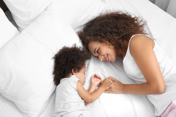 African-American mother with sleeping daughter lying on bed