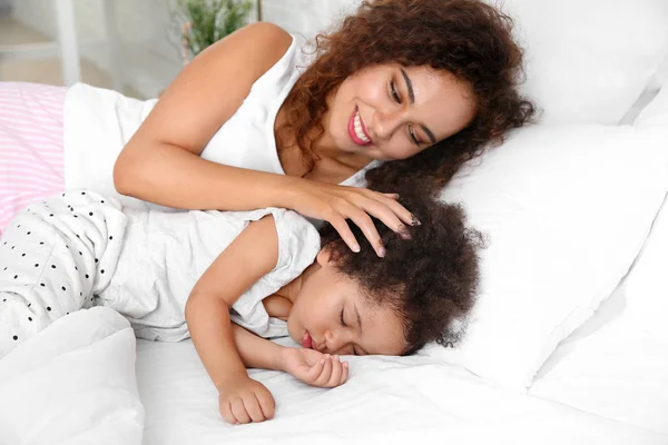 African-American mother with sleeping daughter lying on bed — Stock Photo, Image