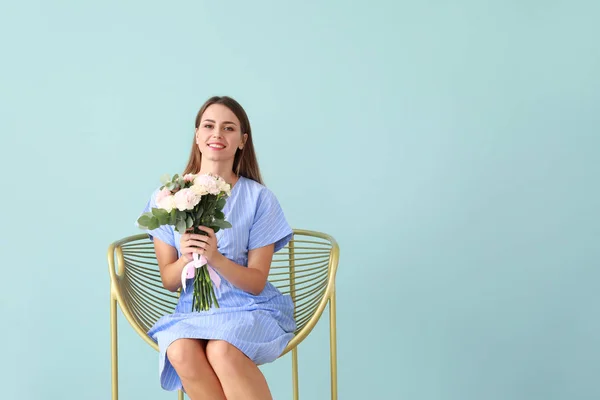 Beautiful young woman with bouquet of carnation flowers sitting in armchair on color background — Stock Photo, Image