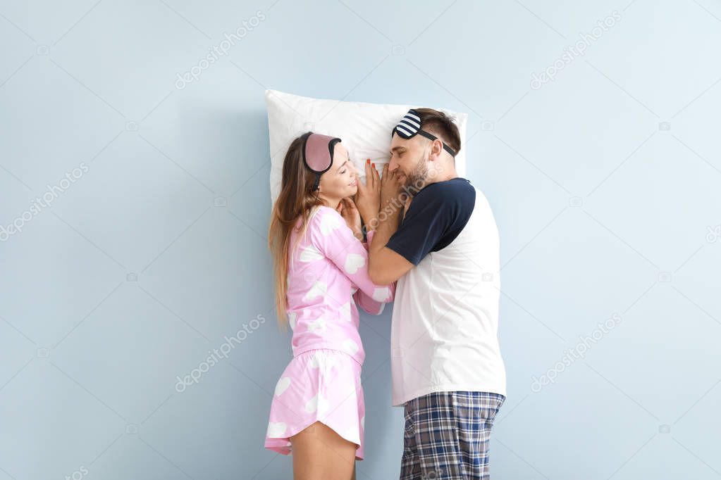 Young couple with pillow on color background