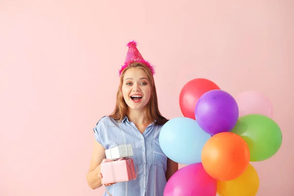 Mujer feliz con regalos y globos de cumpleaños en el fondo de color — Foto de Stock