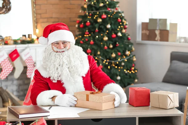 Weihnachtsmann verpackt Geschenke im weihnachtlich dekorierten Zimmer — Stockfoto
