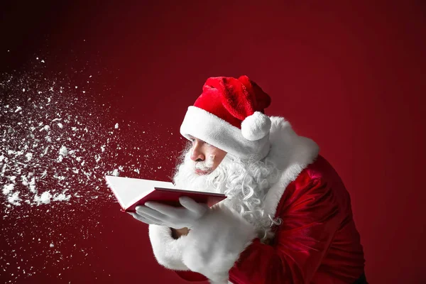 Retrato de Santa Claus con libro soplando nieve sobre fondo de color —  Fotos de Stock