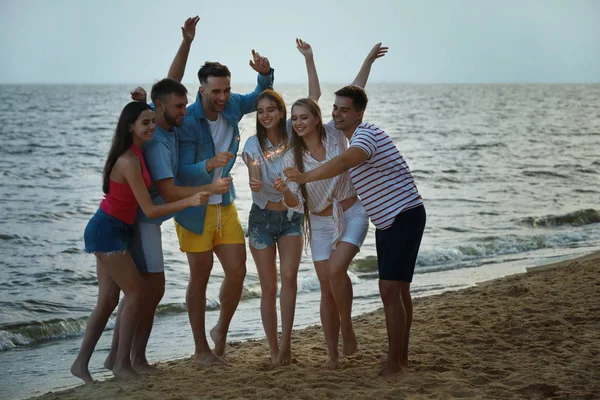 Amigos felices con bengalas en la playa de mar en el resort —  Fotos de Stock