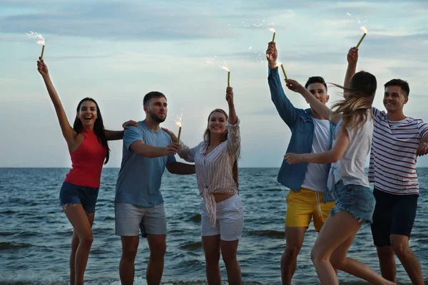 Happy friends with sparklers on sea beach at resort — Stock Photo, Image