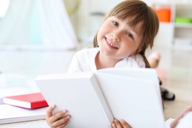 Evde kitap okuyan sevimli küçük bir kız.