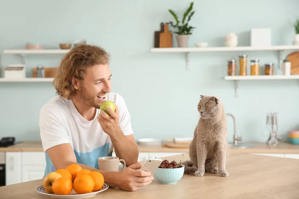 Man eating fruit while sitting in kitchen with cute cat — Stock Photo, Image