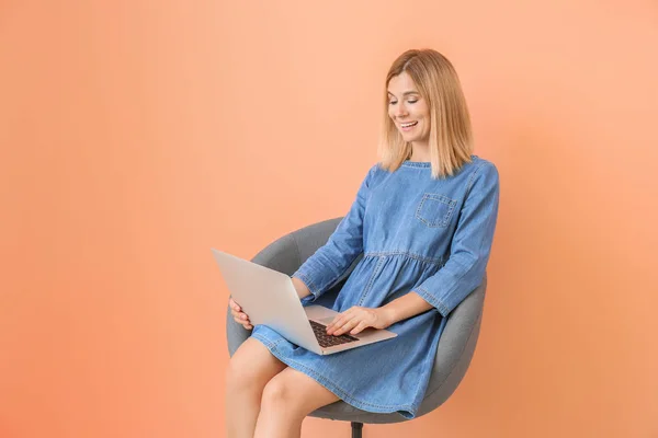 Femeie fericită cu laptop așezat în fotoliu pe fundal color — Fotografie, imagine de stoc