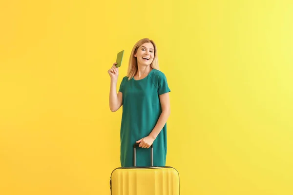 Mujer hermosa feliz con equipaje y pasaporte en el fondo de color — Foto de Stock
