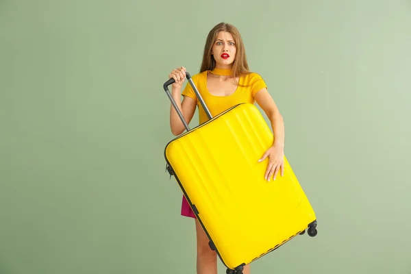 Mujer joven asustada con maleta sobre fondo de color — Foto de Stock