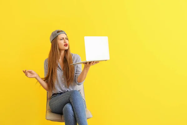 Troubled young woman with laptop sitting on chair against color background — Stock Photo, Image