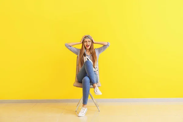 Feliz joven sentada en la silla cerca de la pared de color —  Fotos de Stock