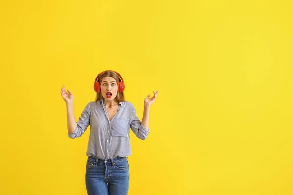 Schockierte junge Frau hört Musik auf farbigem Hintergrund — Stockfoto