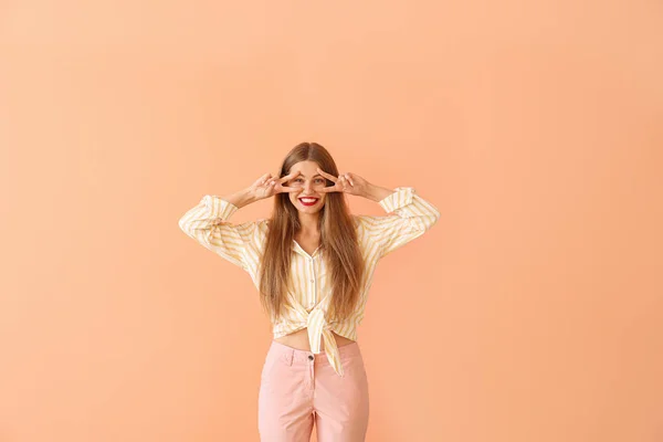 Glückliche junge Frau zeigt Siegesgeste auf farbigem Hintergrund — Stockfoto