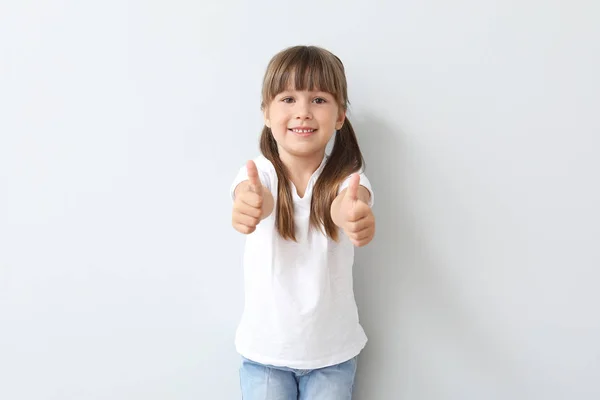 Little girl in stylish t-shirt showing thumb-up on light background — Stock Photo, Image