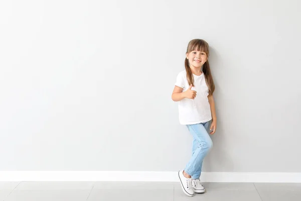 Little girl in stylish t-shirt near light wall — Stock Photo, Image