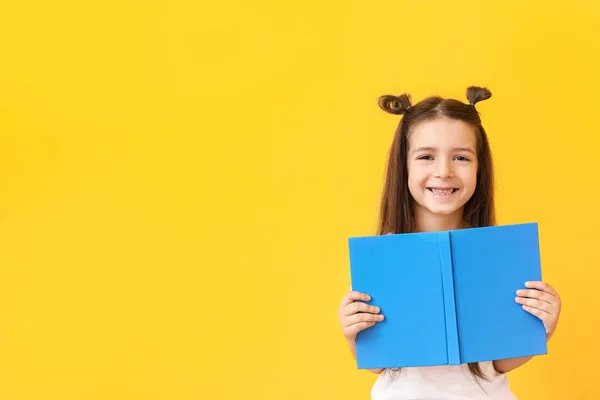 Nettes kleines Mädchen mit Buch auf farbigem Hintergrund — Stockfoto