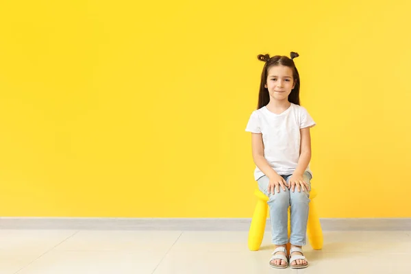 Linda niña en elegante camiseta sentada en la silla contra la pared de color — Foto de Stock