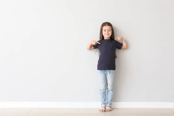 可爱的小女孩指着她的T恤靠近光墙 — 图库照片