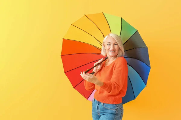 Стильная зрелая женщина с зонтиком на цветном фоне — стоковое фото