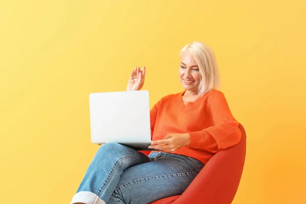 성숙한 여자 와 노트북 앉아 에 의자 대 색상 배경 — 스톡 사진