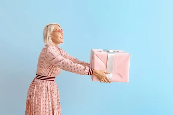 Mujer madura con caja de regalo sobre fondo de color — Foto de Stock