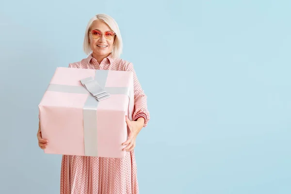 Volwassen vrouw met geschenk doos op kleur achtergrond — Stockfoto