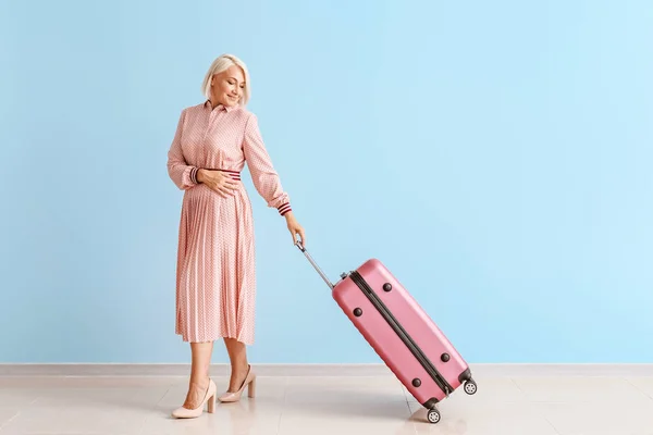 Зрелая женщина с багажом у цветной стены — стоковое фото