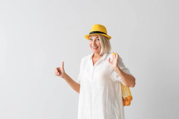 Mature woman with eco bag showing thumb-up on light background — Stock Photo, Image