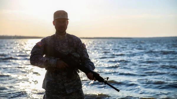 Silhouette di soldato in mimetizzazione con fucile d'assalto vicino al fiume — Foto Stock