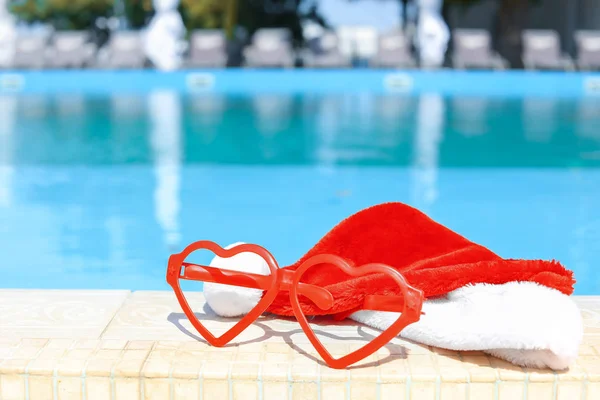 Santa hat and glasses on the edge of swimming pool at resort — Stock Photo, Image