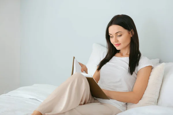 Hermosa joven leyendo libro en el dormitorio — Foto de Stock