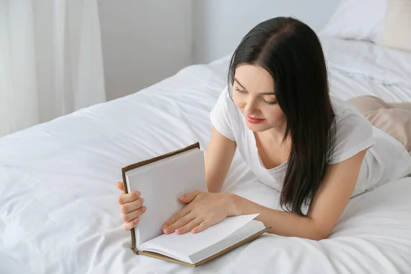 Hermosa joven leyendo libro en el dormitorio — Foto de Stock