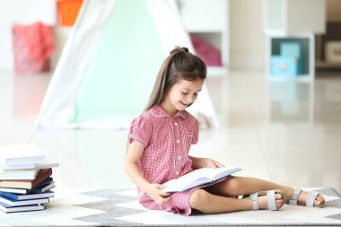 Evde kitap okuyan sevimli küçük bir kız.