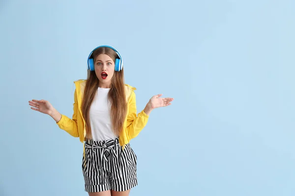 Mujer joven sorprendida escuchando música sobre fondo de color — Foto de Stock