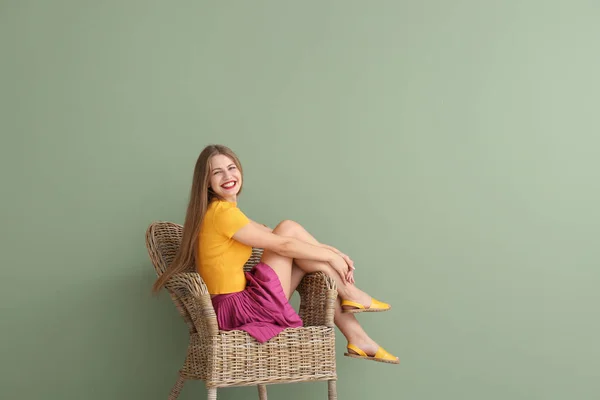 Happy young woman sitting in armchair on color background — Stock Photo, Image