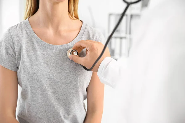 Doctor listening woman's heartbeat in clinic — Stock Photo, Image