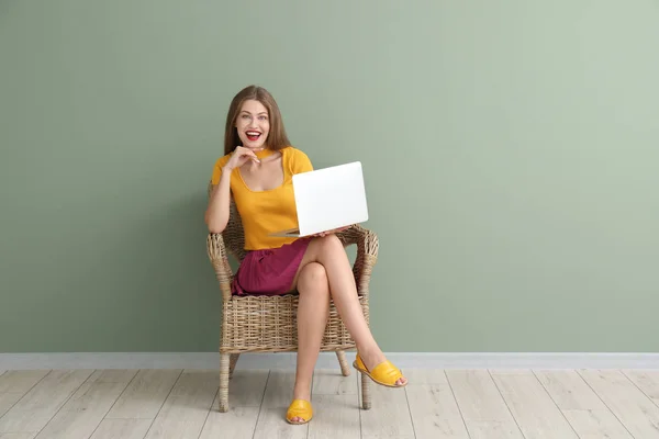 Szczęśliwa młoda kobieta z laptopa siedząc w pobliżu kolor ściany — Zdjęcie stockowe